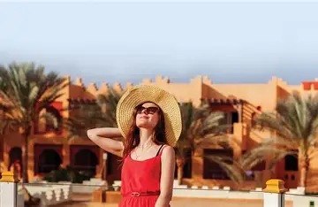 A woman in a red dress and wide-brimmed hat stands outdoors
