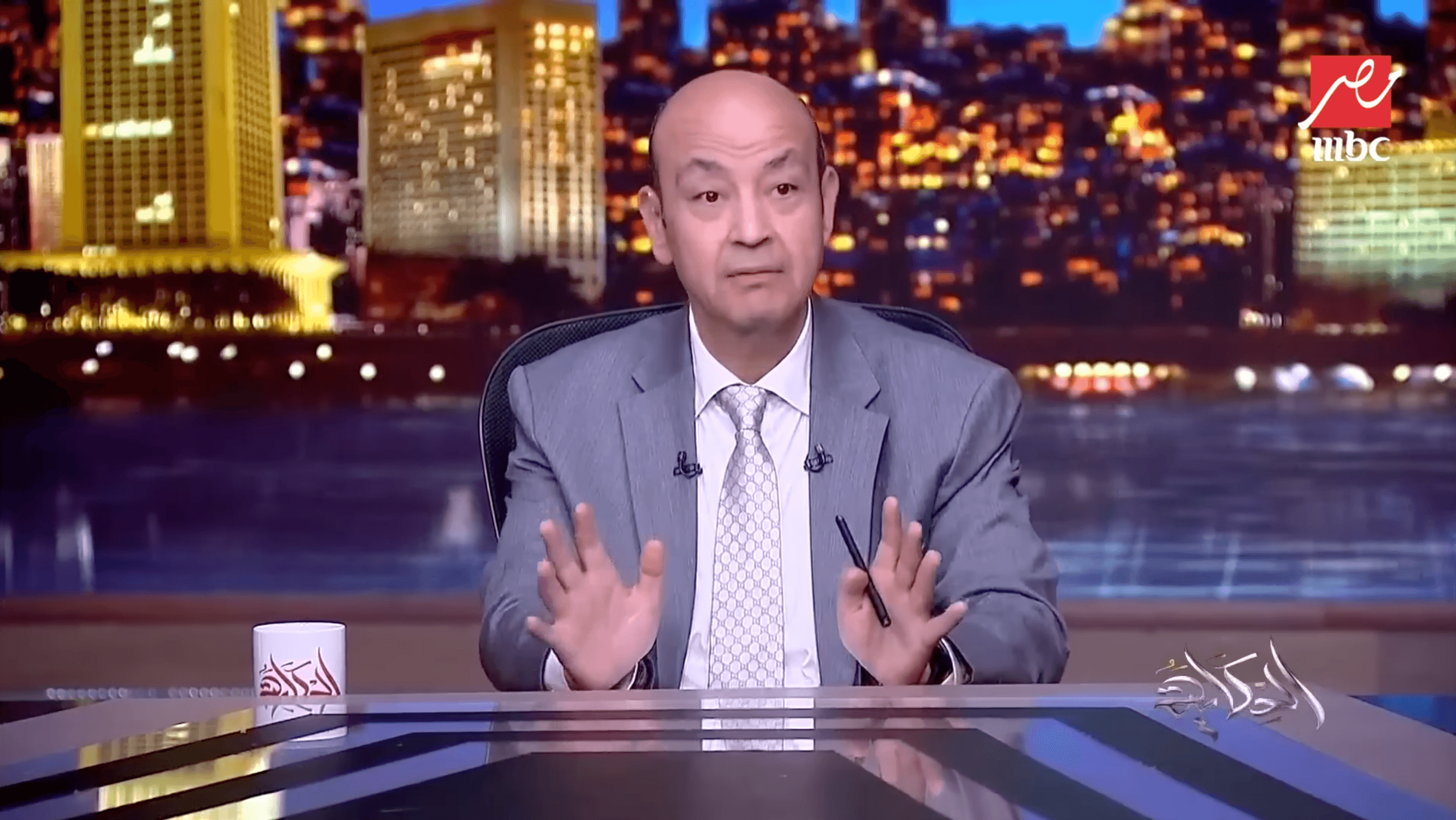 A man in a gray suit sits at a news desk with a cityscape backdrop at night, discussing expert property management. The MBC logo is visible in the top right corner, with Arabic text on the desk and mug.